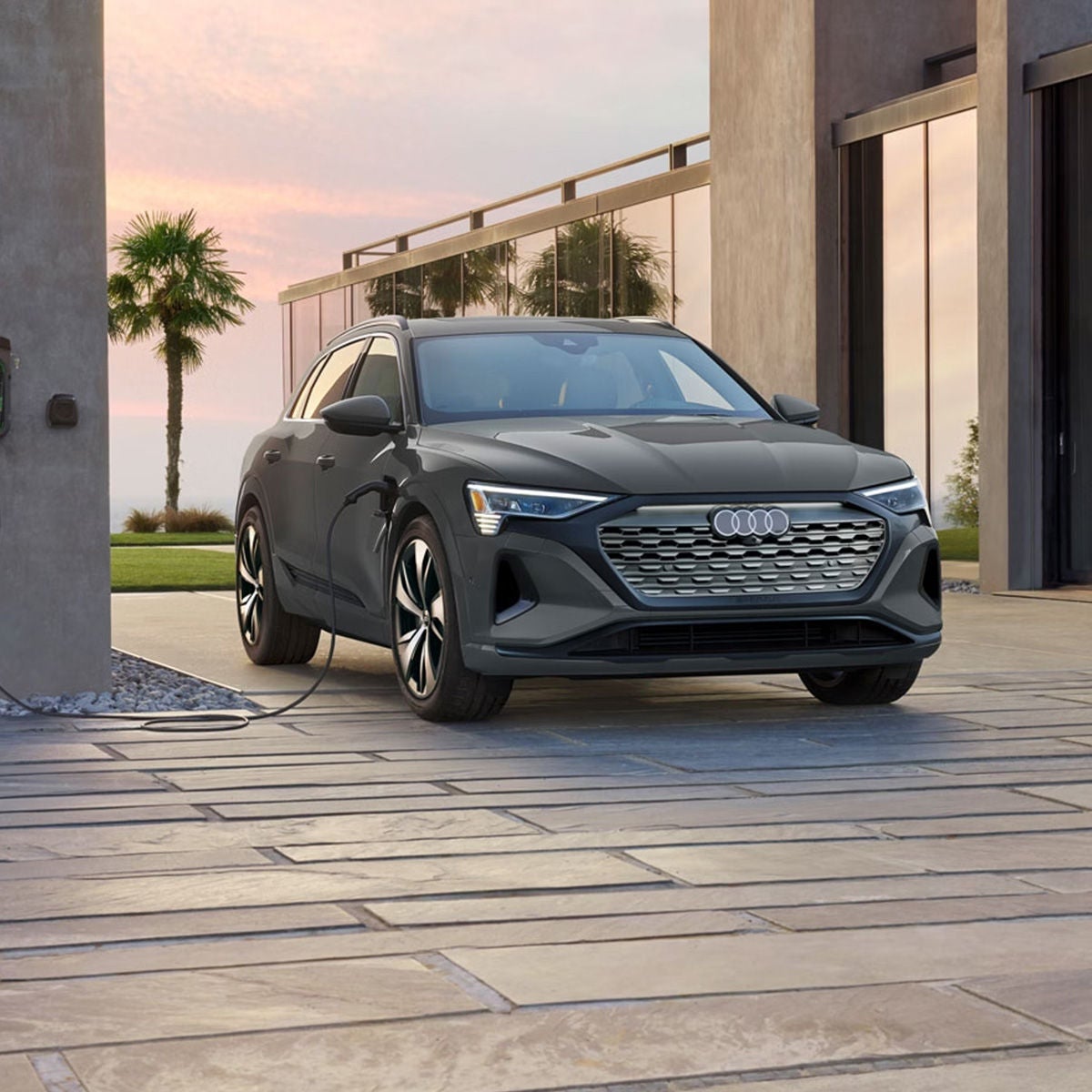 Three-quarter front profile of a gray Audi Q8 e-tron parked and charging on a driveway. 