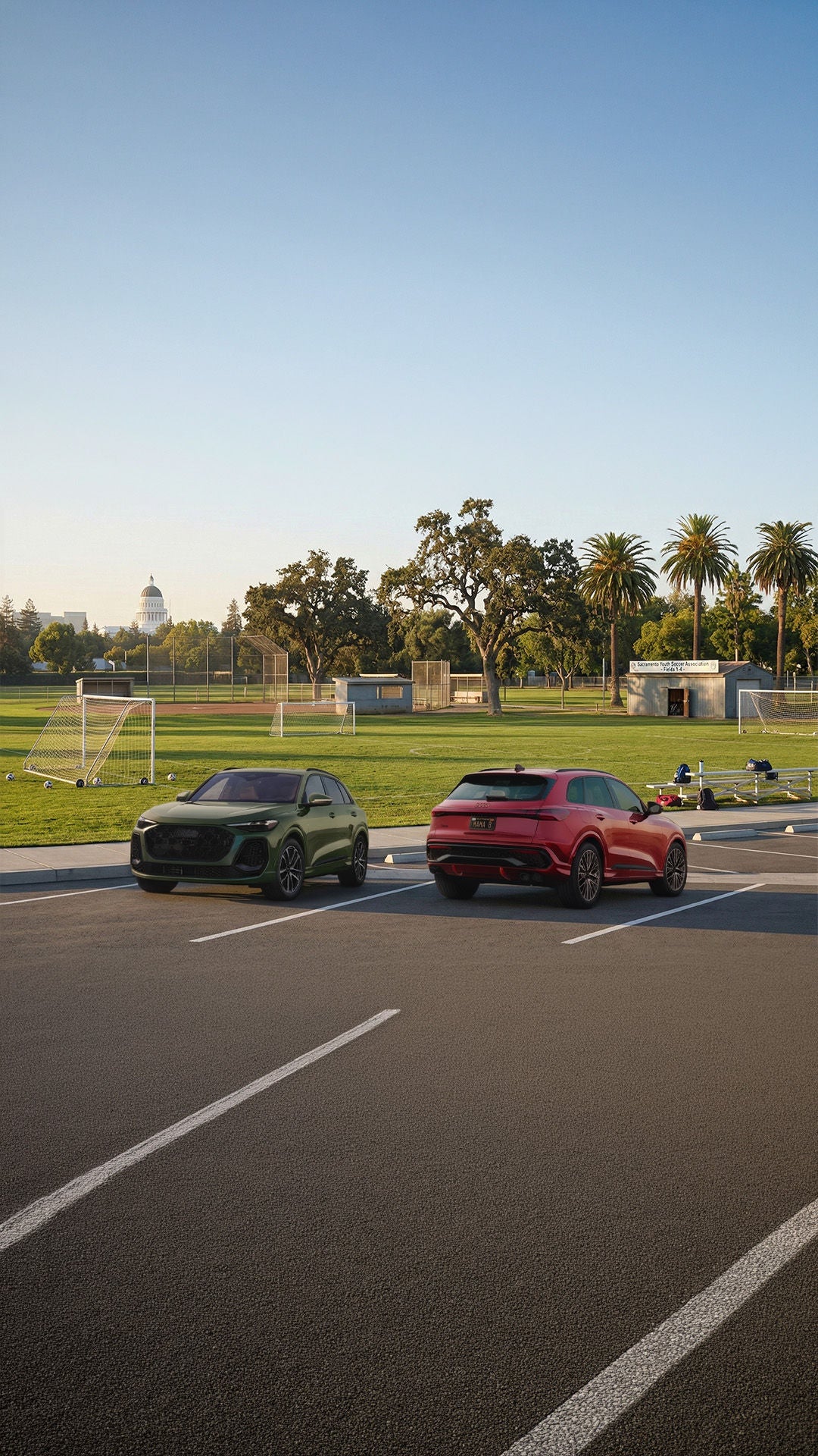 Two 2026 Audi Q5 SUVs parked next to each other next to a soccer field with the Sacramento capital building rising above the trees in the distance.
