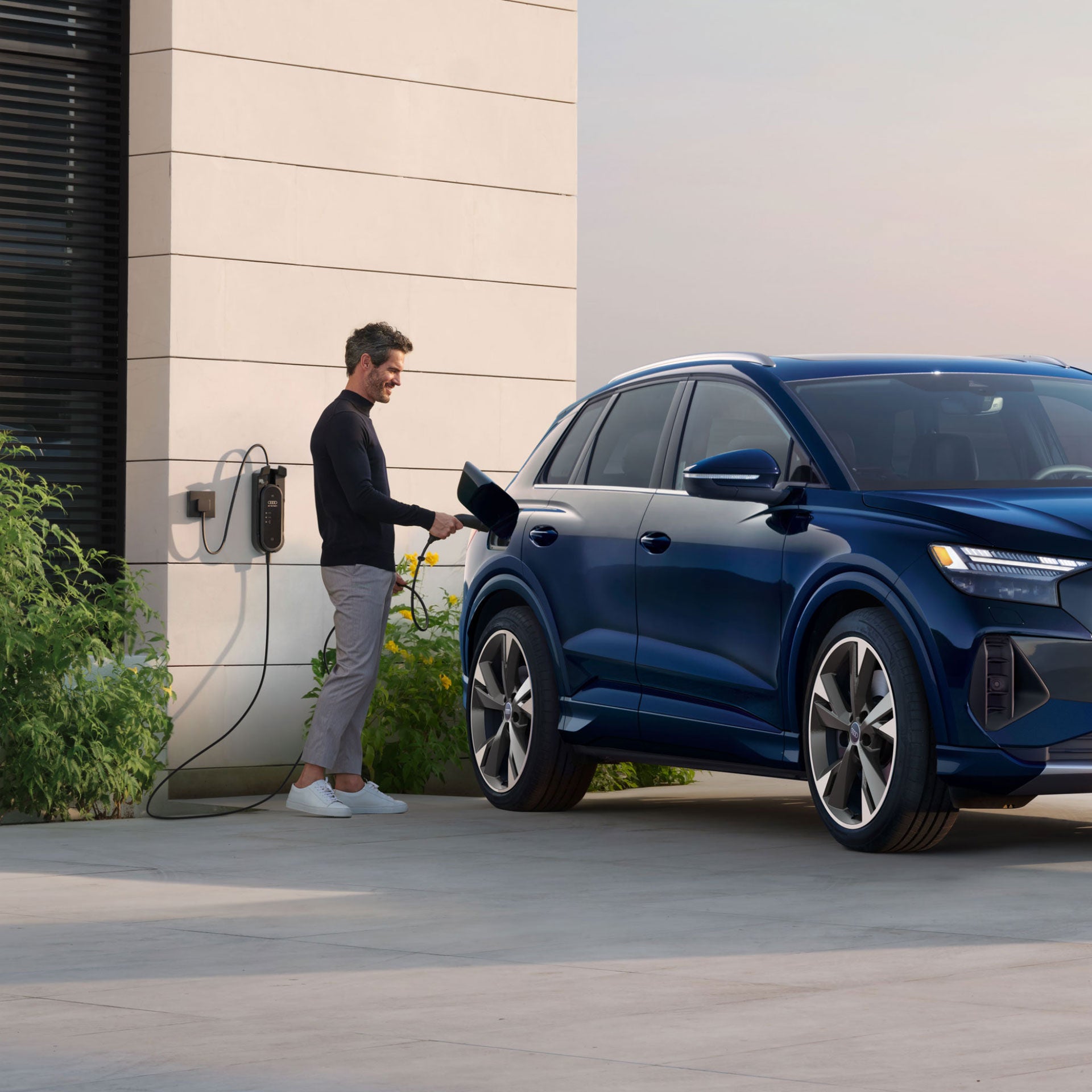 Un homme qui charge son Audi Q4 Sportback e-tron devant une maison moderne.