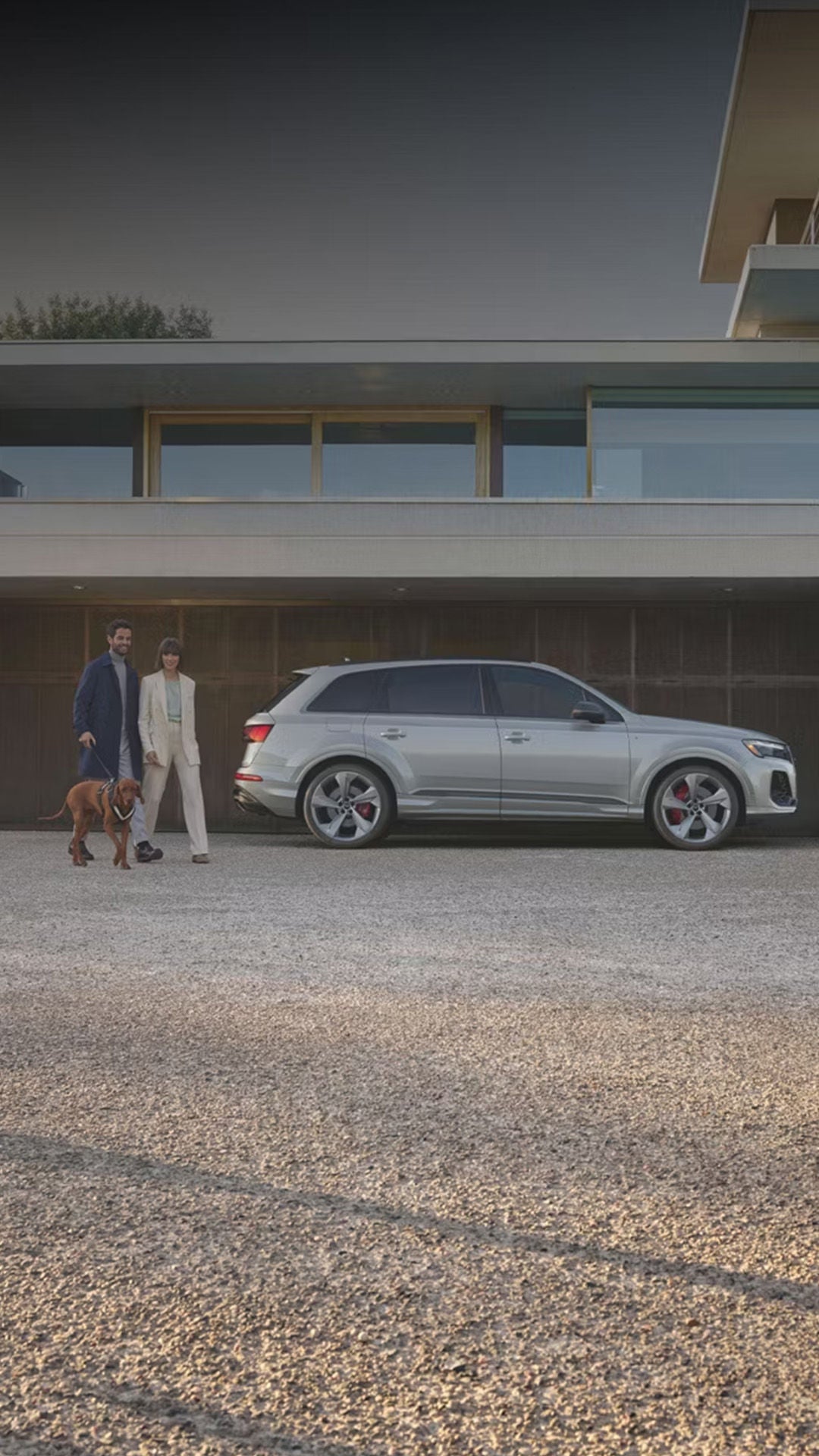 Side profile of the Audi Q7 with a couple walking their dog next to it.