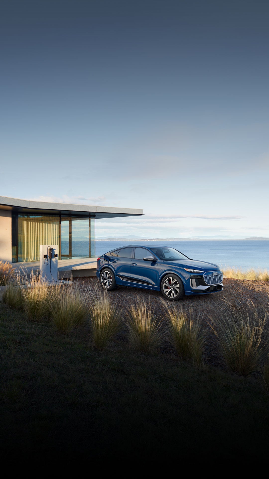 Three-quarter side view of the Audi SQ6 Sportback e-tron parked and charging by a waterfront home.