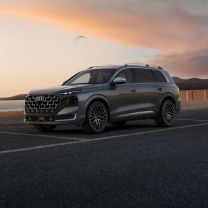 Grey Audi SQ9 driving through a modern city street, shown from the side profile.