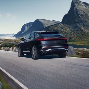 Rear side view of an Audi SQ5 Sportback driving through a rural landscape.