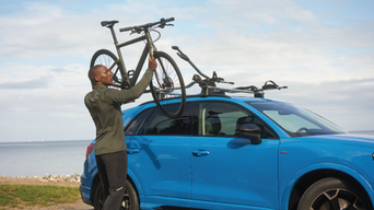 Man putting bike onto roof rack of a blue Audi Q3