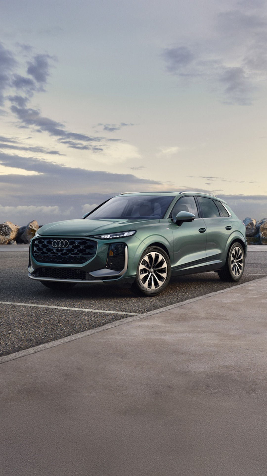 All new 2026 Audi Q3 parked under a cloudy sky with a rock wall behind it