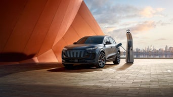 Three-quarter front-view of the Audi SQ6 e-tron parked and charging by a modern building.