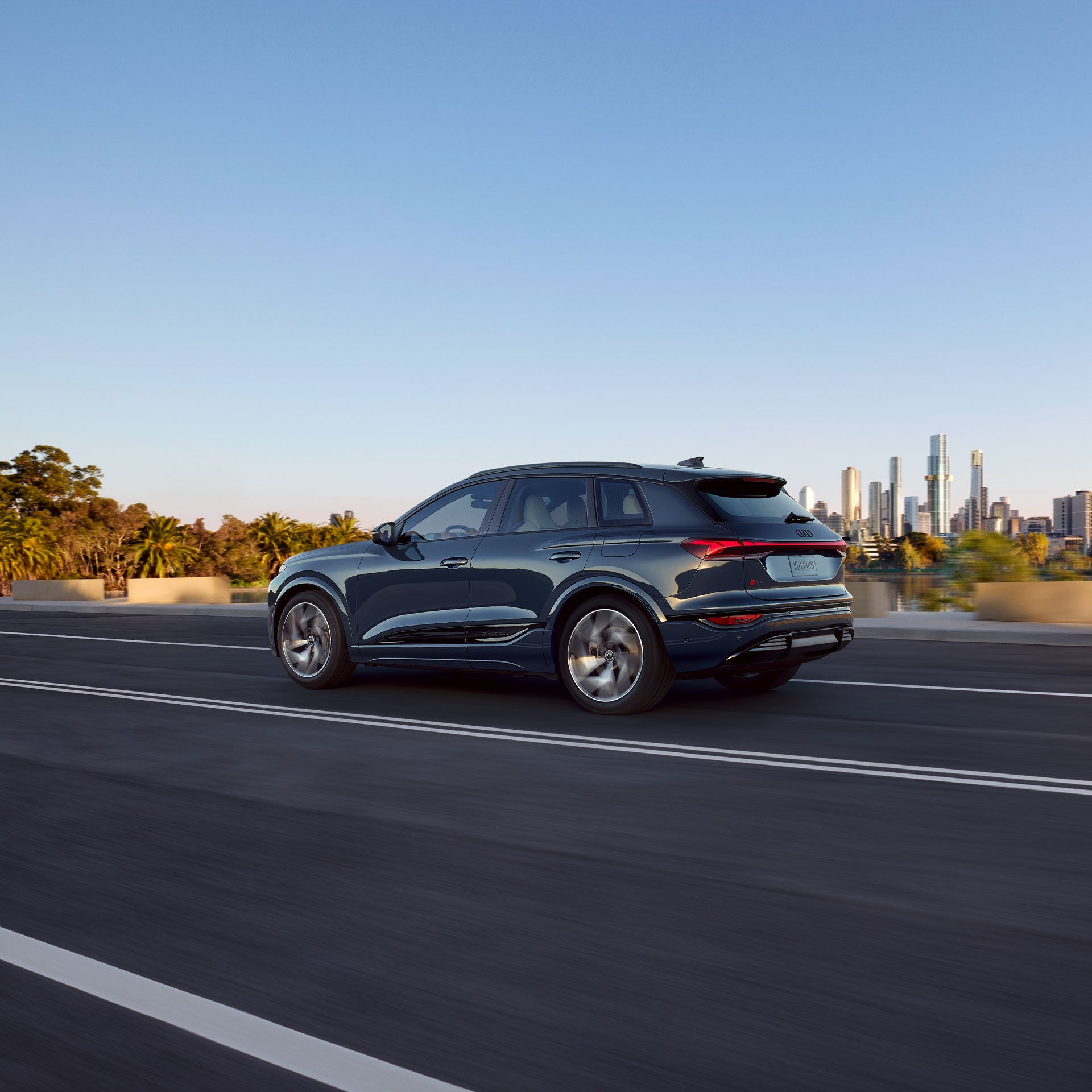 A black 2024 Audi A6 driving by an urban structure.