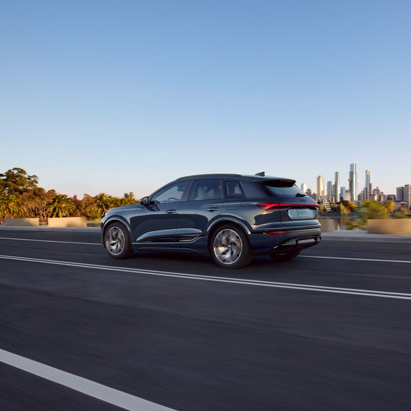 Three-quarter side view of a blue Audi Q6 e-tron accelerating on a city road.