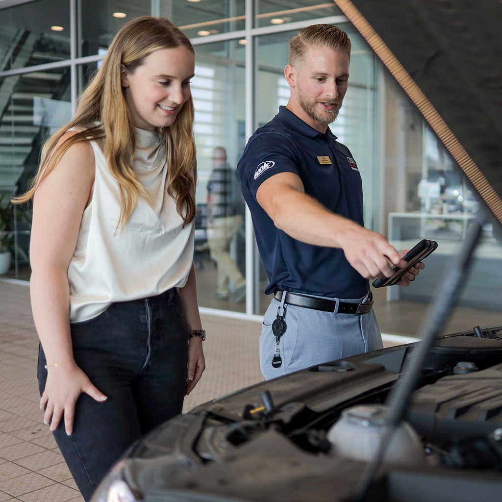 Audi employee showing features of a vehicle with hood open to a customer.