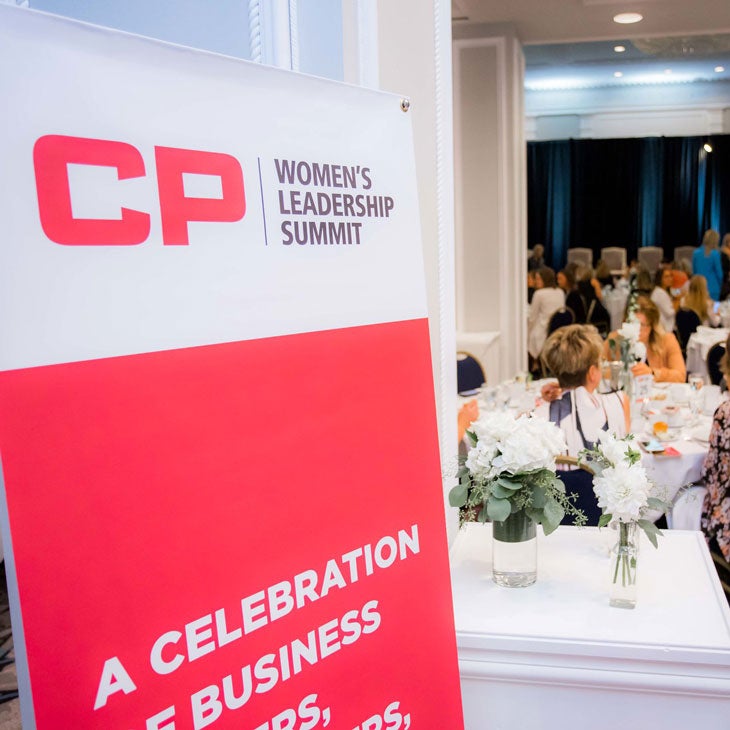 Close-up photo of signage displayed at the CP Women's Leadership Summit with women leaders in the background sitting and talking.