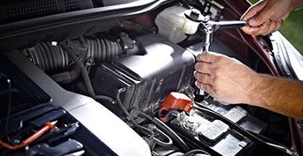 Service technician servicing vehicle with hood open.