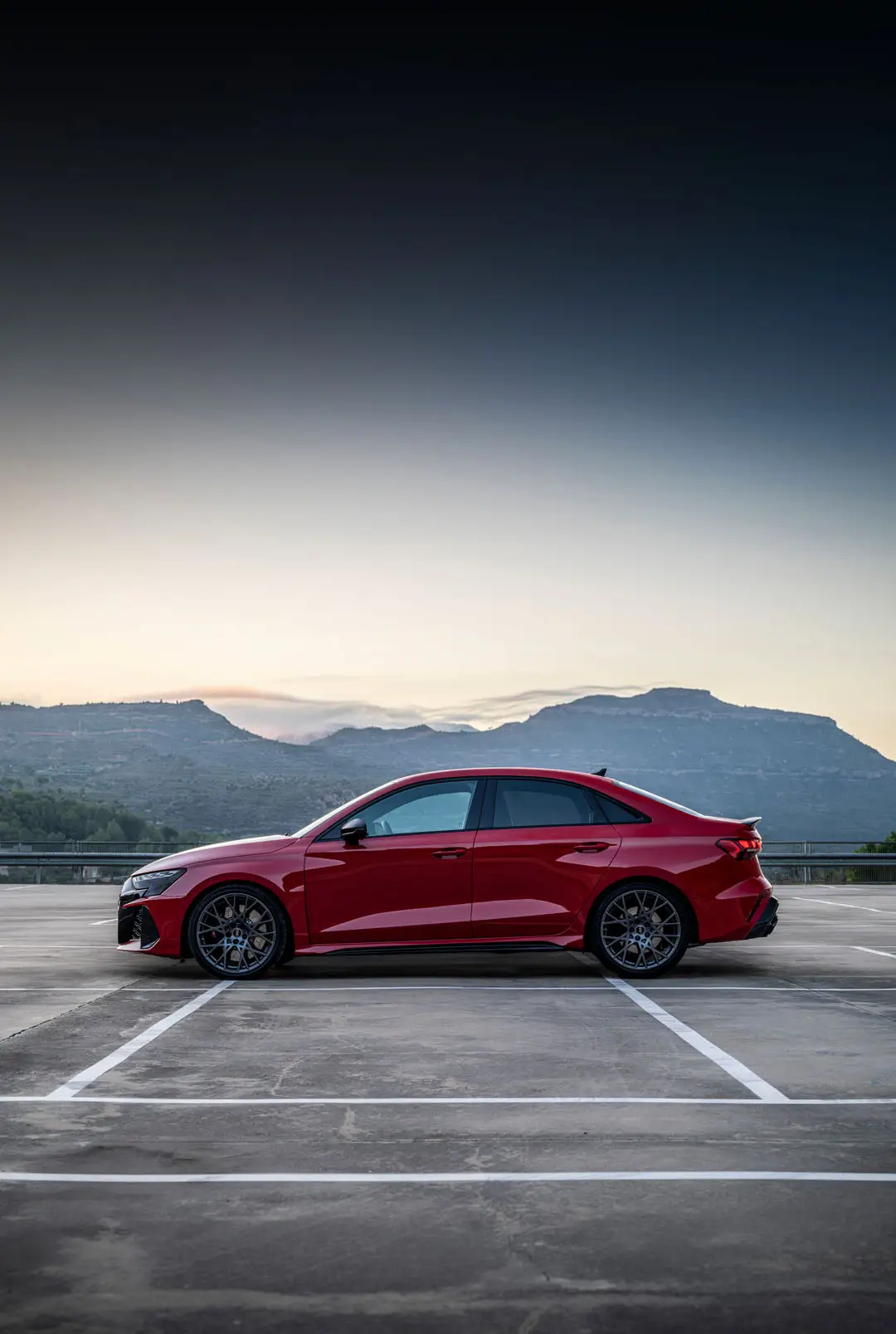 Vue de profil de l'Audi RS3 rouge devant un décor de montagne.