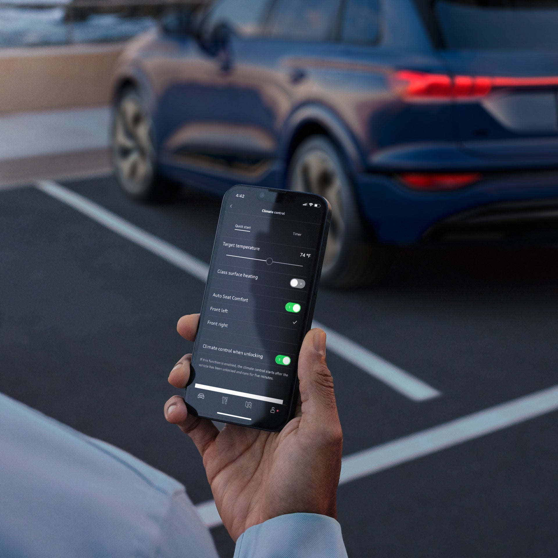 A woman’s hand gripping a smartphone opened to the myAudi app, while standing in front of an Audi. 