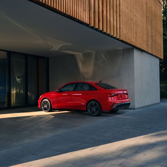 Three-quarter side view of the Audi A3 parked by a modern building.