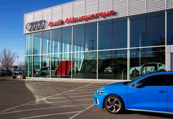 Woman holding glasses standing beside an Audi, looking to the right, smiling at the sun.