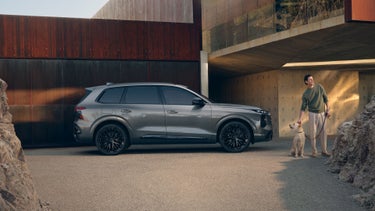 Side profile of the Audi SQ7 parked by a modern building with a person and dog standing nearby.
