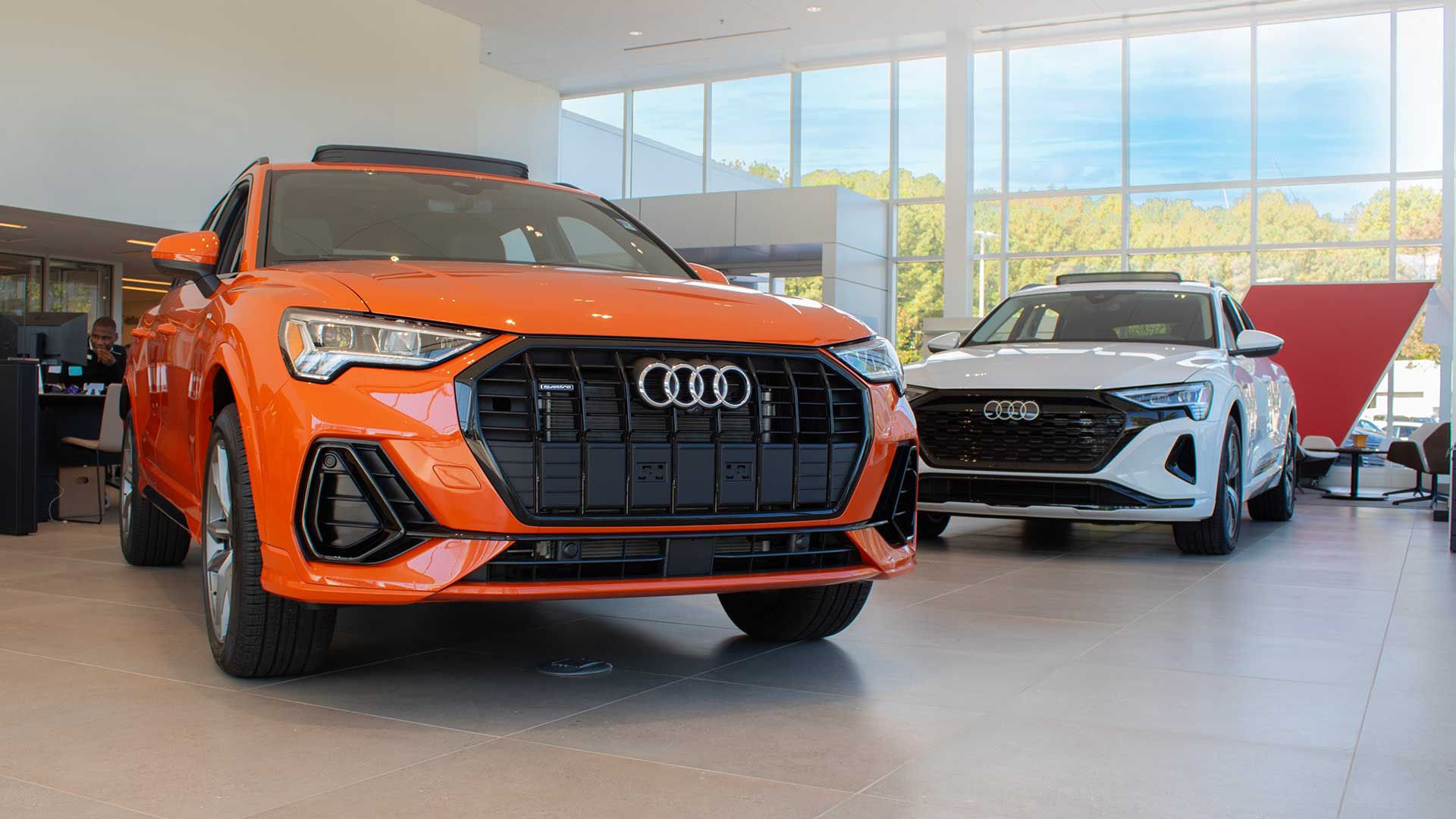 Audi sales specialist walking with a customer through the showroom. The sales specialist is handing the customer a key fob for an Audi vehicle.