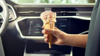 A person holding a melting ice cream cone inside an Audi.