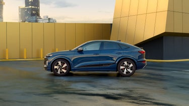 Side profile of the Audi SQ6 Sportback e-tron parked by a modern building.