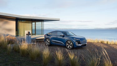 Three-quarter side view of the Audi SQ6 Sportback e-tron parked and charging by a waterfront home.