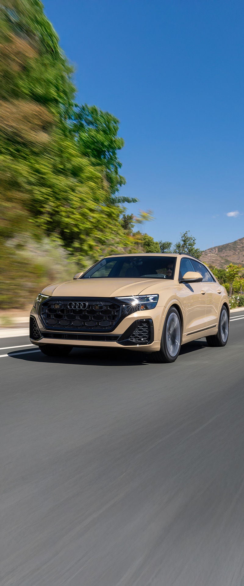 2025 Audi Q8 trim in tan driving around curve on highway with background blurred