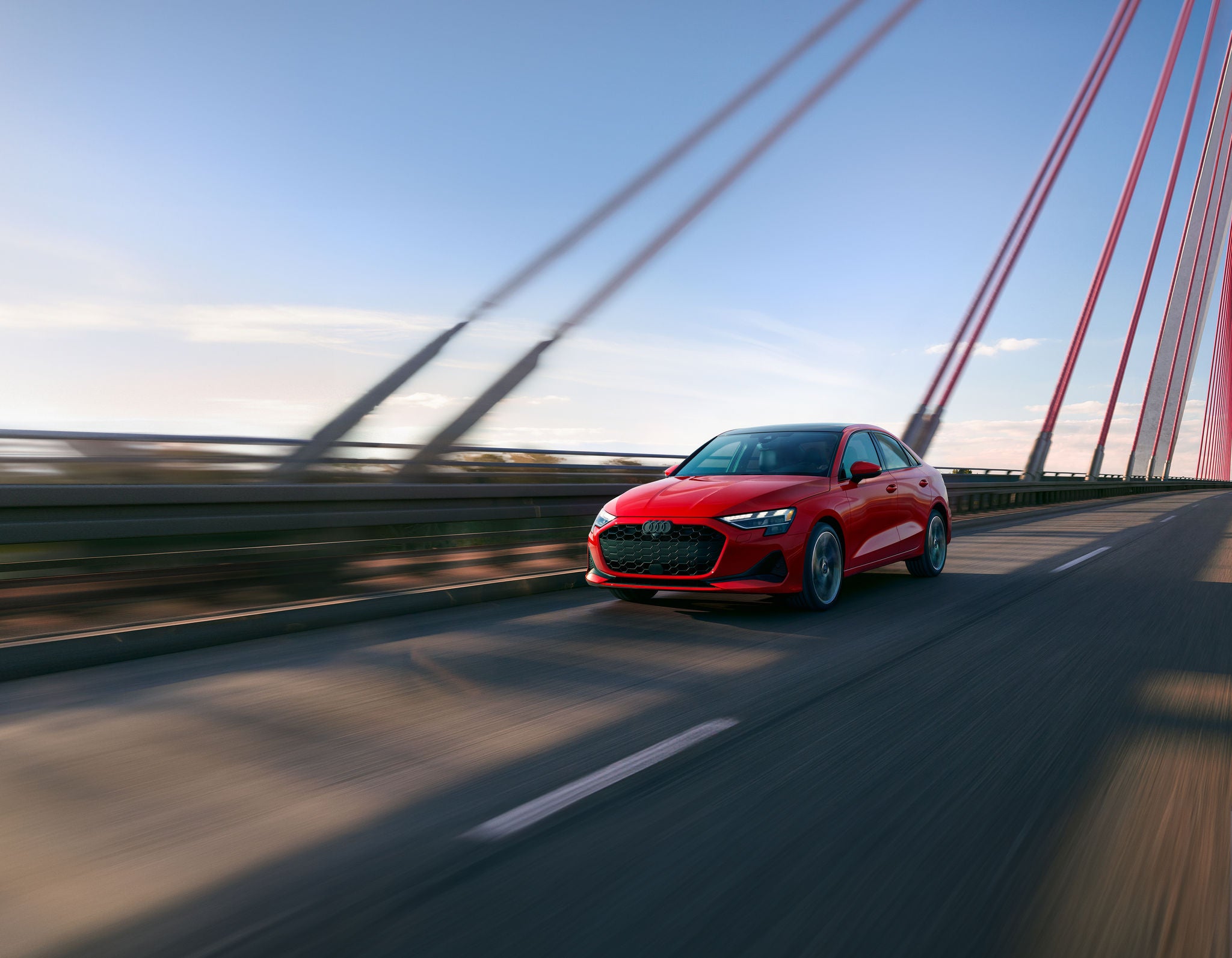 Red 2025 Audi A3 Premium driving on a suspension bridge.
