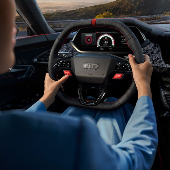 Over-the-shoulder view of a person driving the Audi RS e-tron GT driving on a road. 