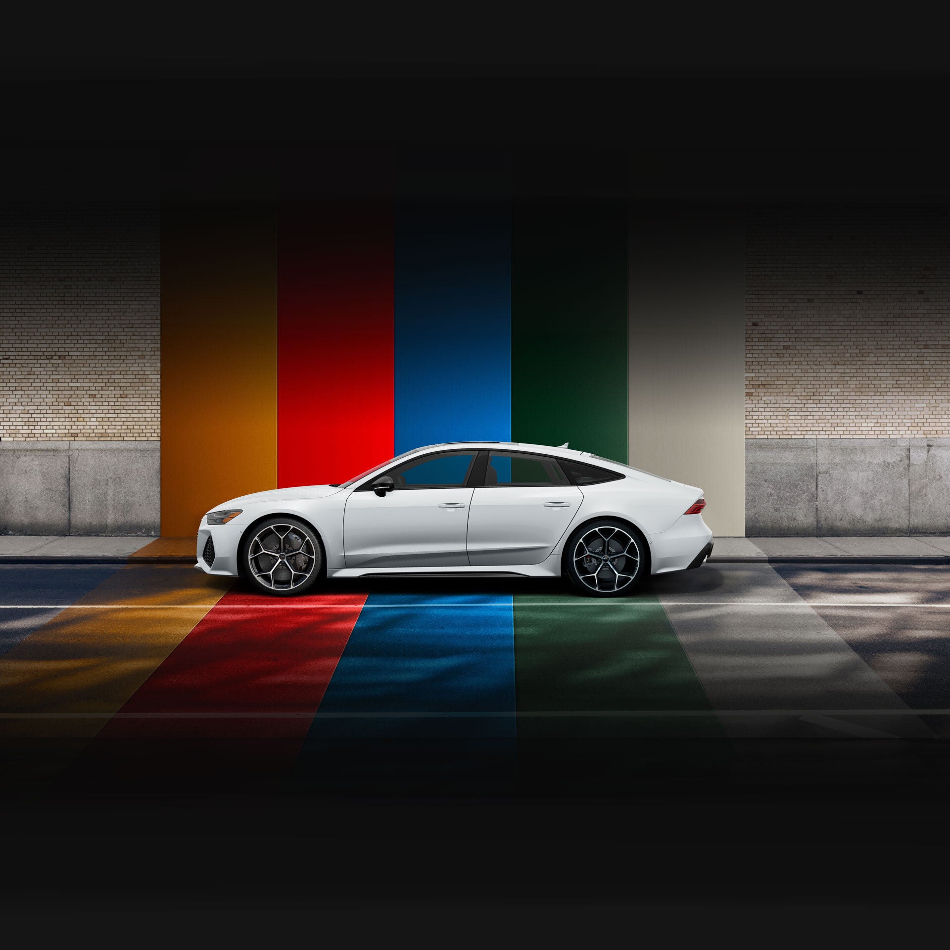 Side profile of a silver Audi RS 7 parked in front of a brightly-striped wall. 