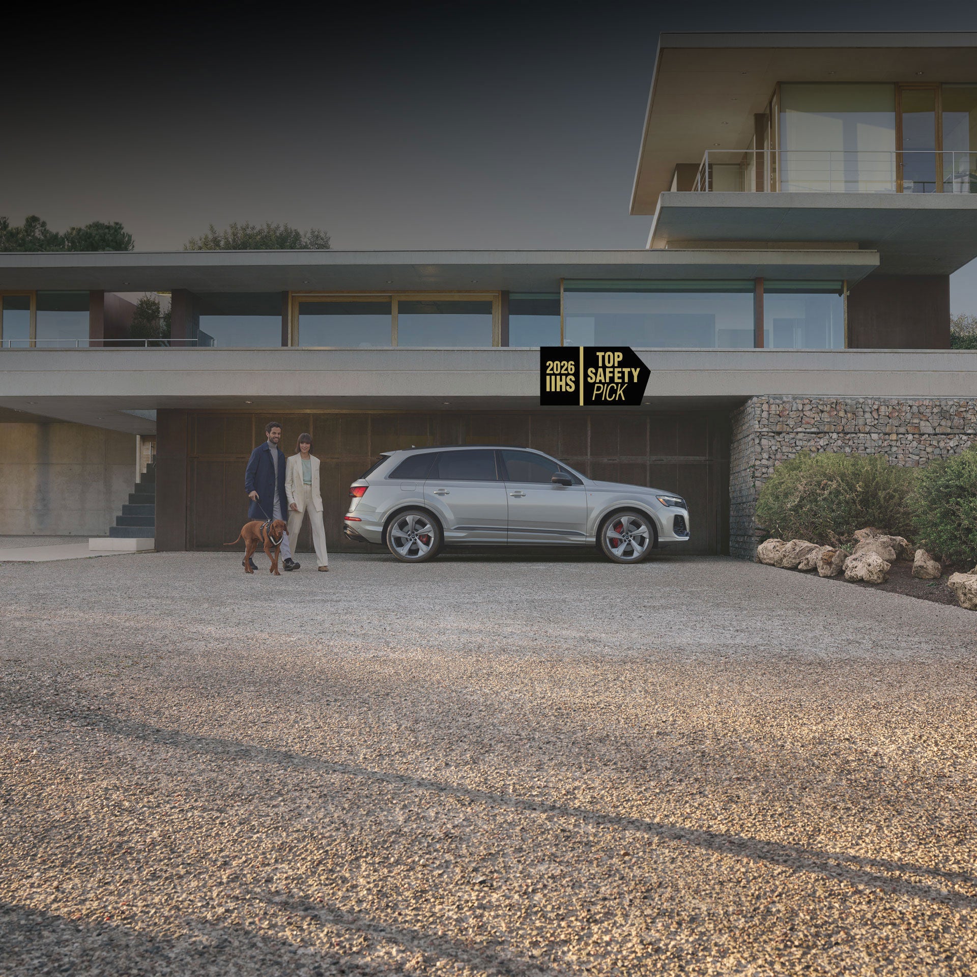 Side profile of the Audi Q7 with a couple walking their dog next to it. 2026 IIHS Top Safety Pick badge is in the top right corner.