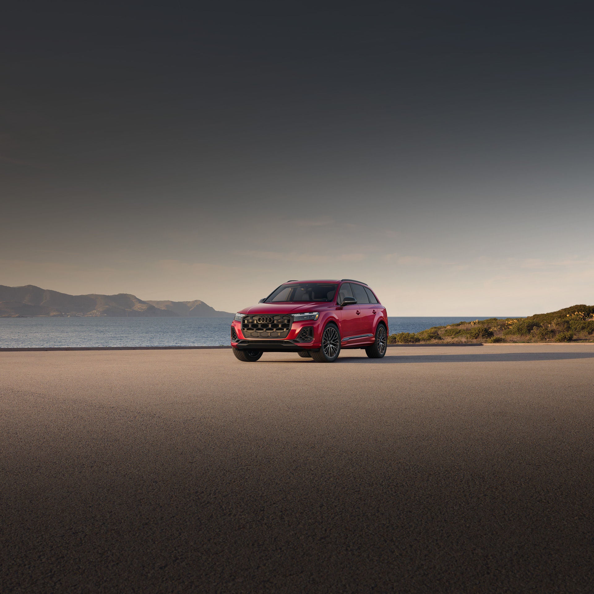 Three-quarter front view of a red Audi SQ7 parked by a waterfront.