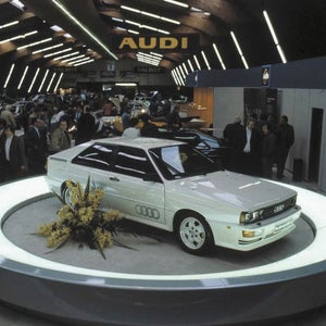 Three-quarter side view of the Audi Quattro parked on a pedestal with people surrounding it.