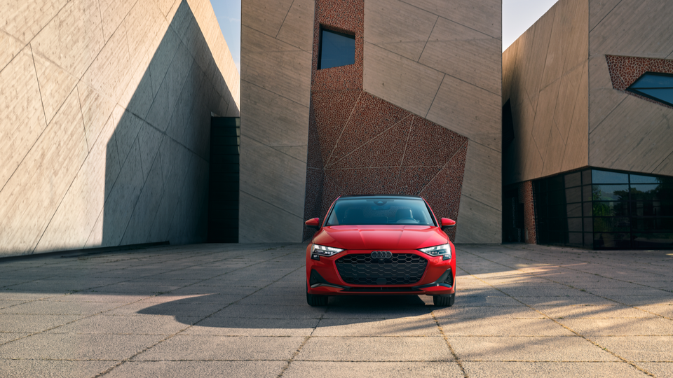 Image of a red Audi a3 parked in front of brown and beige concrete wall.