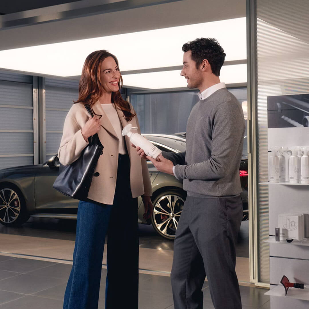 An Audi service representative assists a smiling customer in a bright Audi dealership.