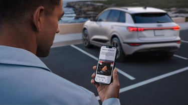Over-the-shoulder view of a person holding a phone, showing the remote climatization feature on the myAudi app.