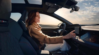 A woman gets into an Audi driving experience vehicle. The instructor stands next to the vehicle on the passenger side.