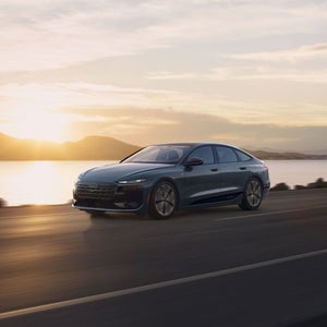 Three-quarter side view of the Audi A6 e-tron accelerating on a waterside road.
