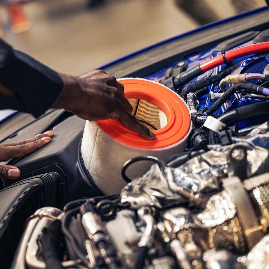 Audi service technician lifting an air filter out from underneath the roof of a vehicle.