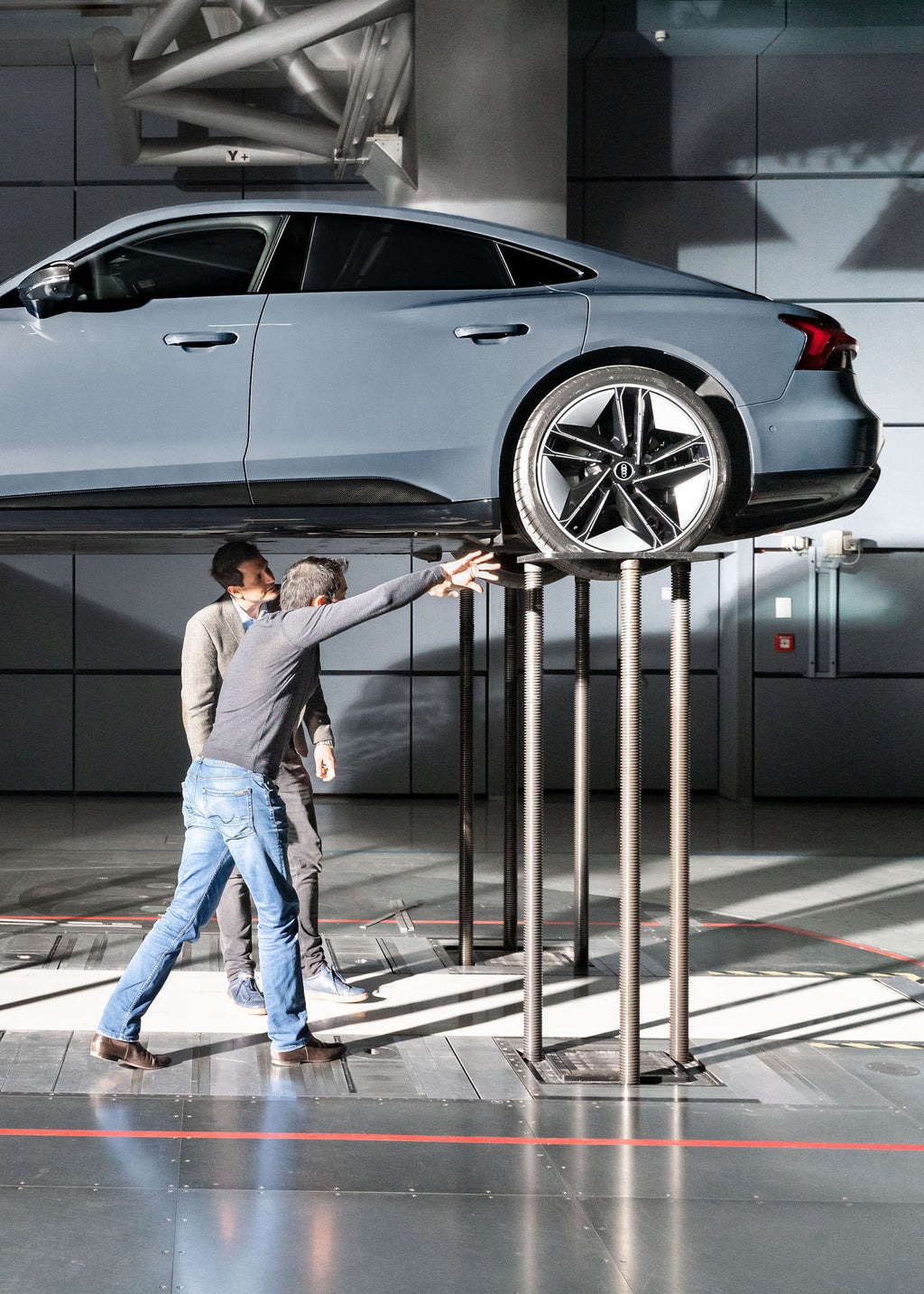 Two Audi aerodynamicists inspect the underbody of an Audi RS e-tron GT on a raised platform.