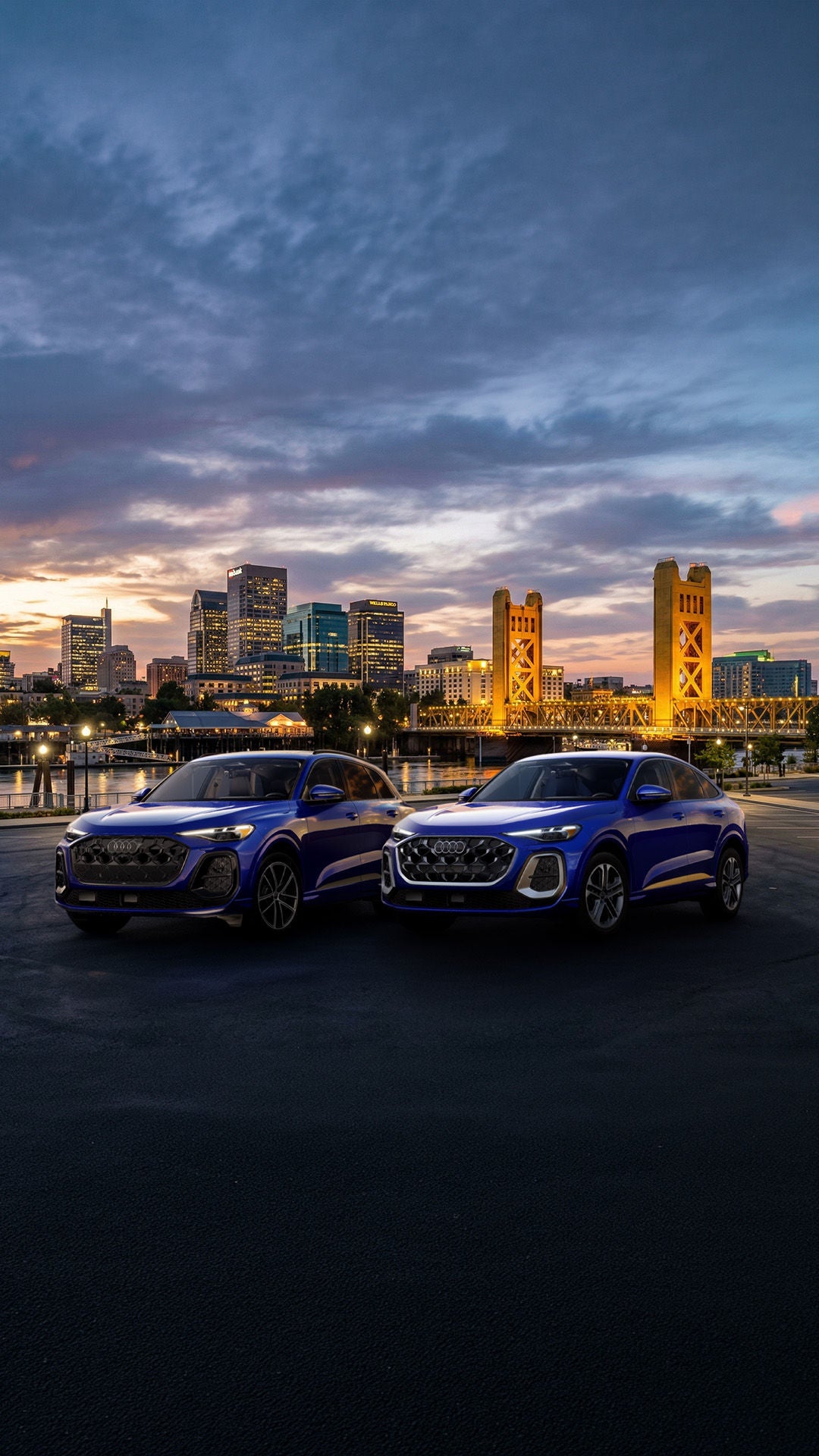 Two 2026 Audi Q5 trim levels parked next to each other infront of the Sacramento skyline at sunset.