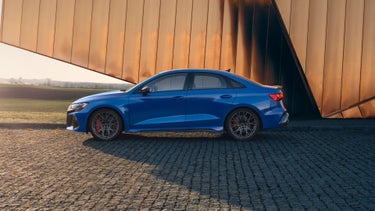 Side profile of the Audi RS 3 parked in front of building.