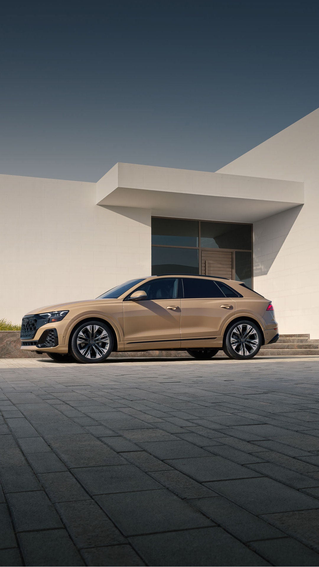 Side profile of the Audi Q8 parked in front of a modern home.