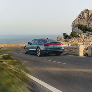 Three-quarter rear view of the Audi S6 e-tron accelerating on a waterside road.