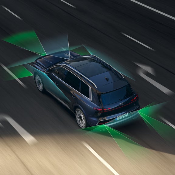 The Audi Q9 SUV, viewed from a diagonal angle above on a four-lane road. From the rear and the front, green and blue vectors divide the areas behind and in front of the vehicle.