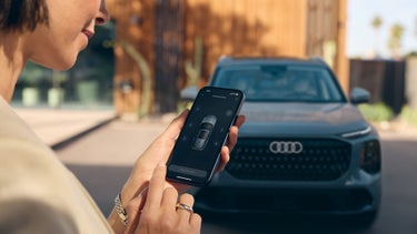 Over-the-shoulder view of a person using the Audi smart entrance feature with an Audi Q7 parked in the background.