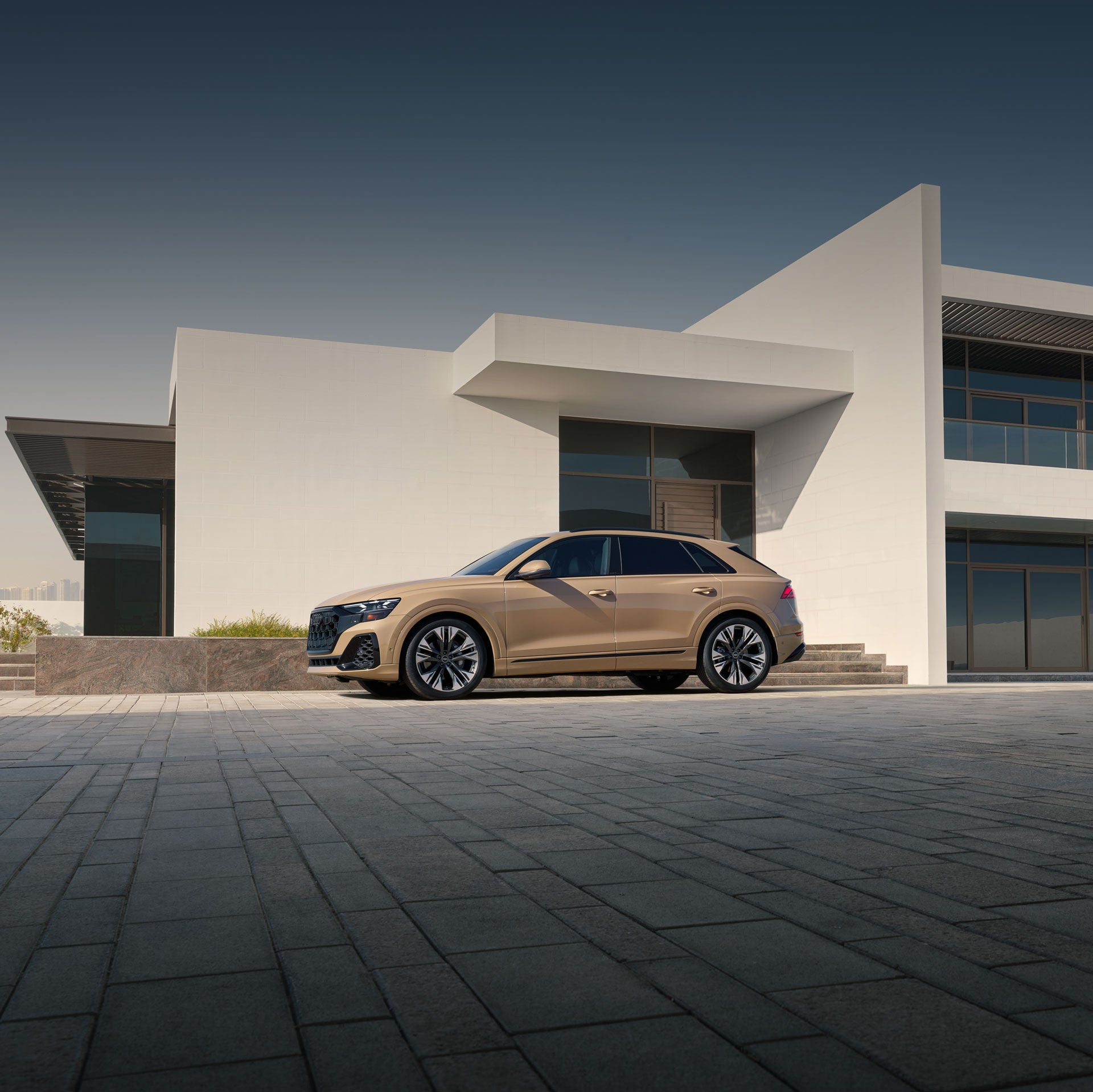 Side profile of the Audi Q8 parked in front of a modern home.