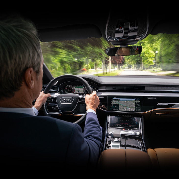 Interior over the shoulder view of a man driving an Audi vehicle.
