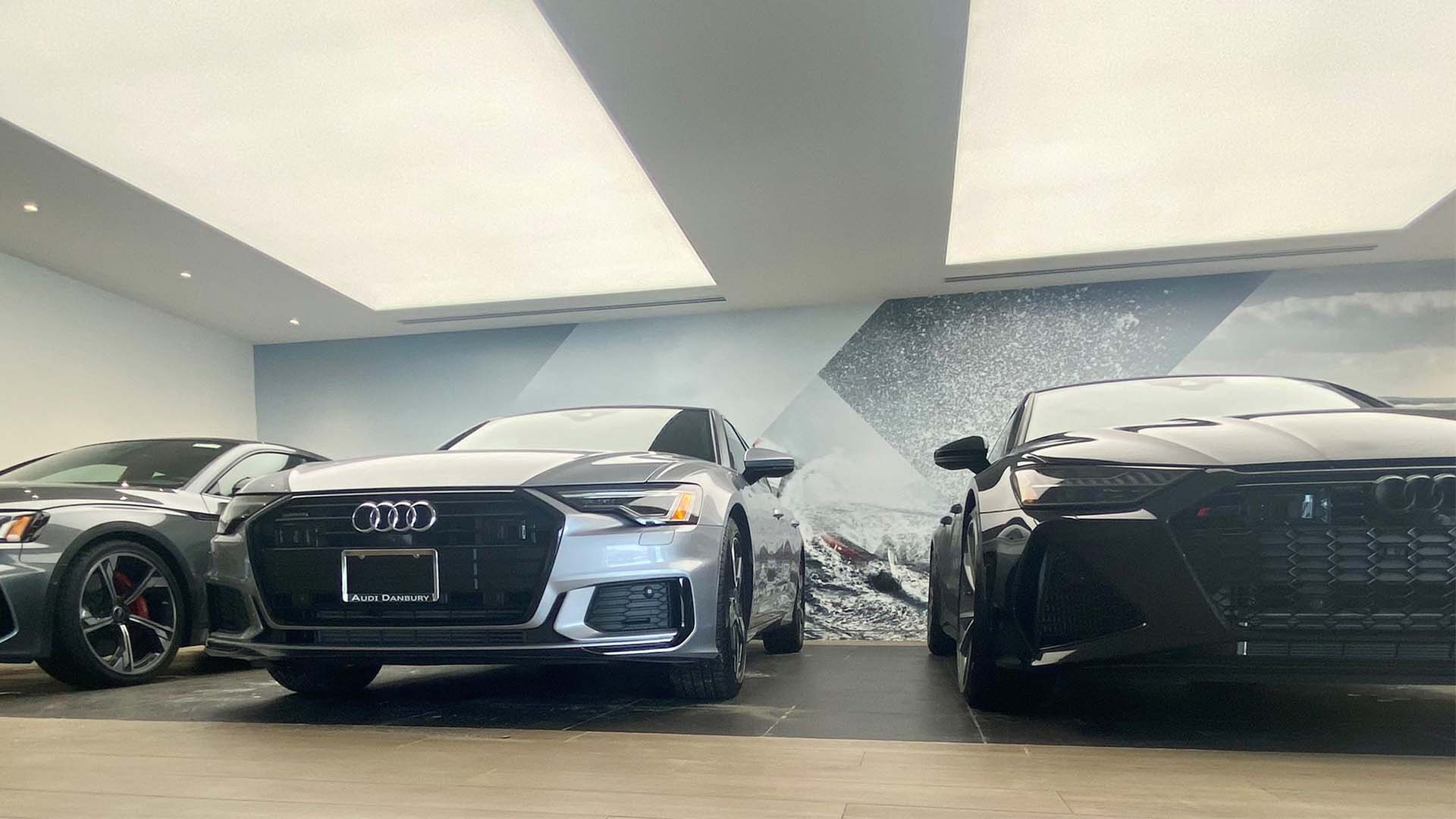 3 people walking through an Audi showroom looking at vehicles.