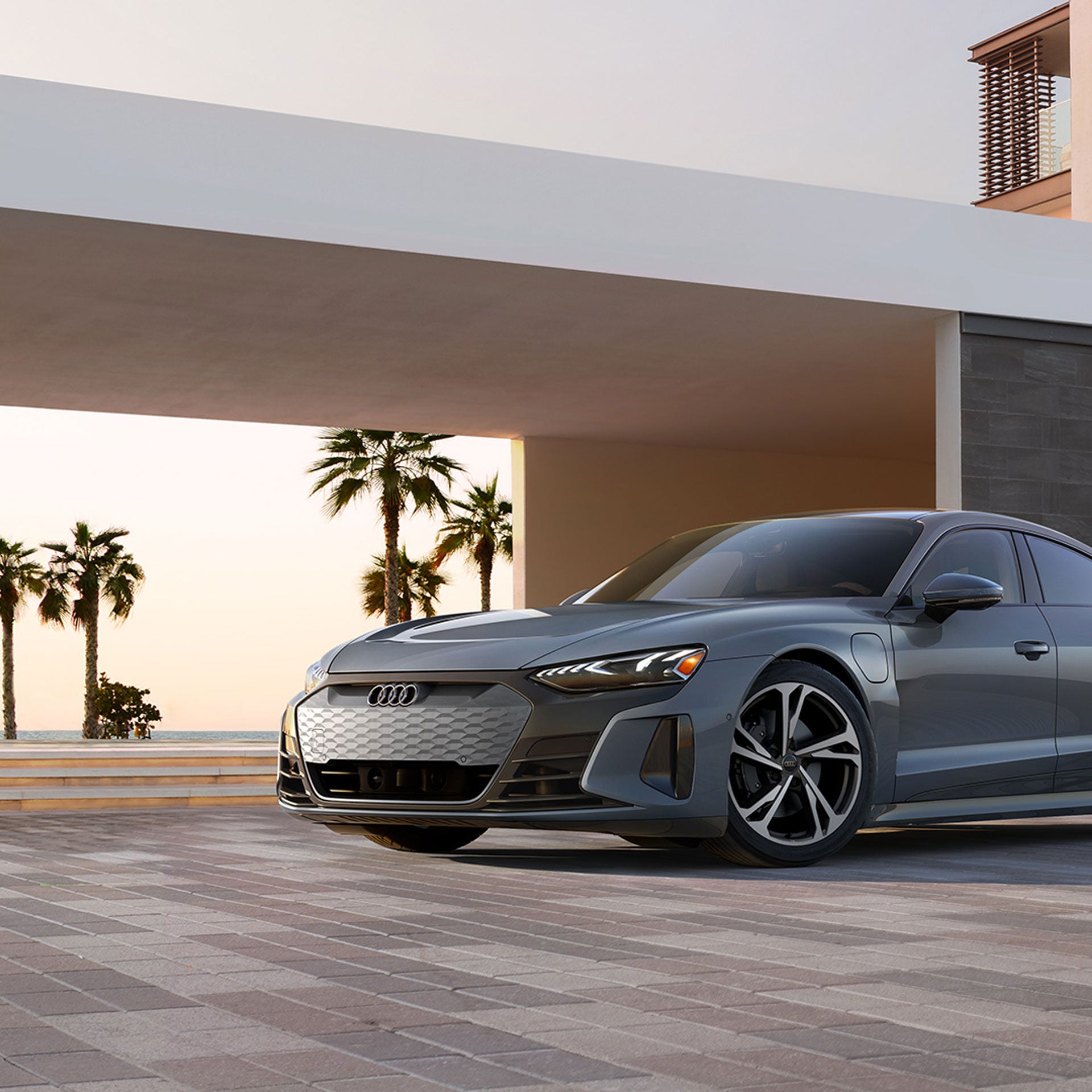 Three-quarter front view of a grey Audi e-tron GT parked in front of a modern house.