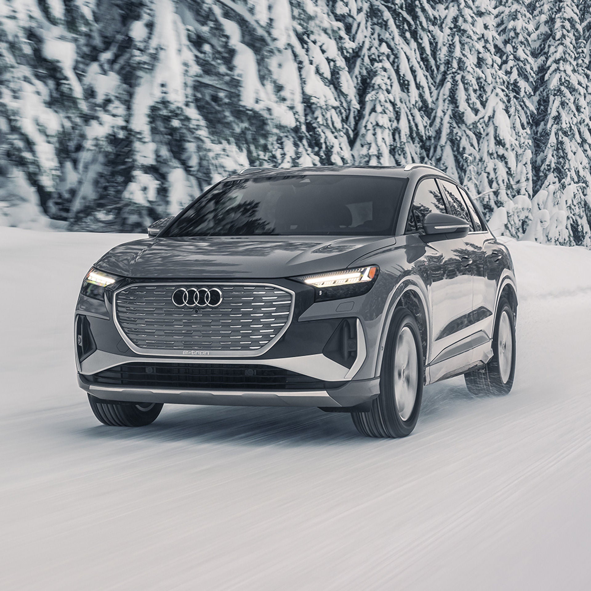 Three-quarter front profile of the Audi Q4 e-tron accelerating on a snowy road.