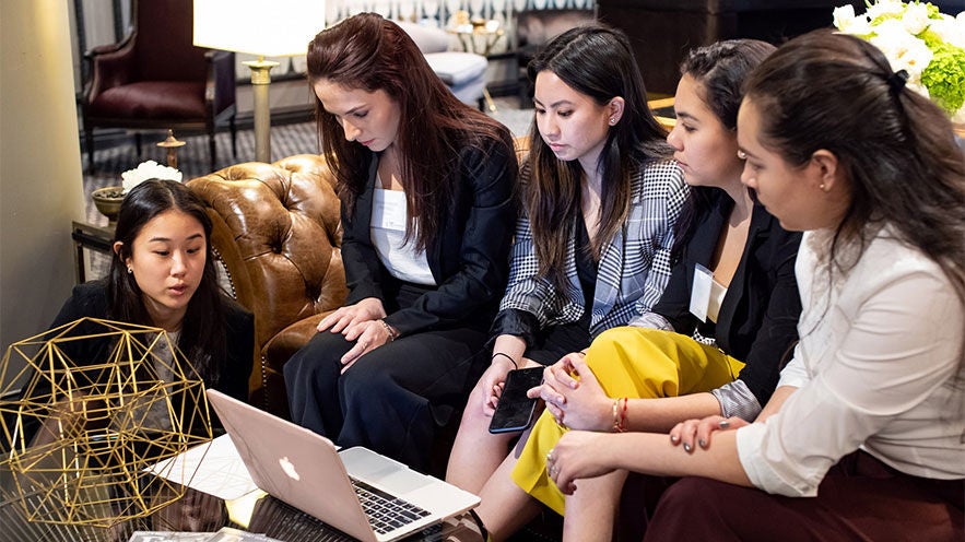 A group of women sitting on a couch, working on a project together.